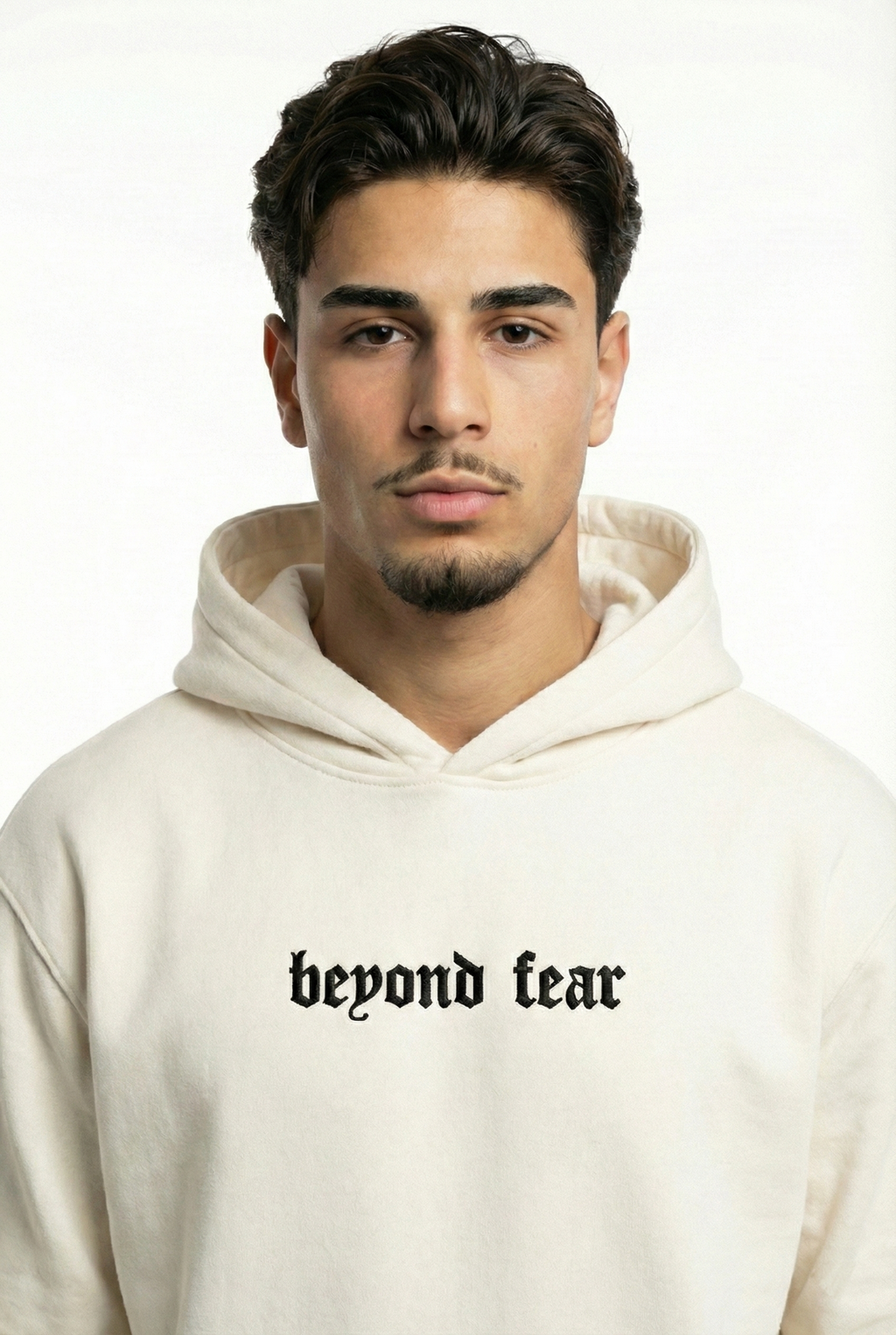 Close-up portrait of a man with dark hair and a beard wearing an off-white hoodie, featuring black beyond fear gothic text embroidered on the chest.